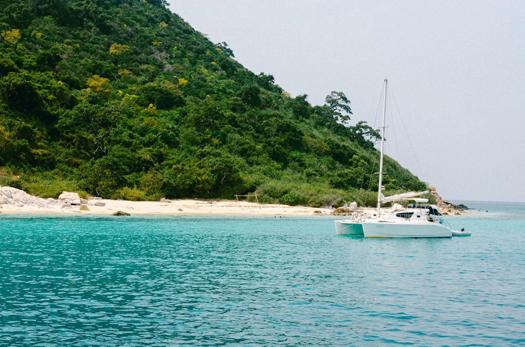 A sailboat anchored near a sandy beach in a protected tropical anchorage