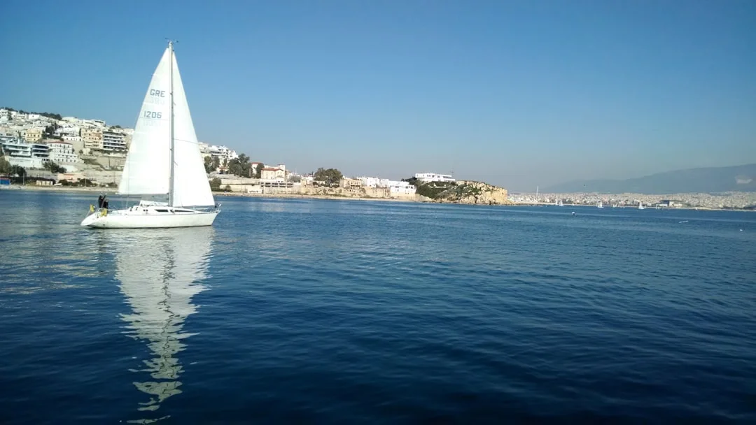 Sailing yacht approaching the Greek coastline with green hills and clear water