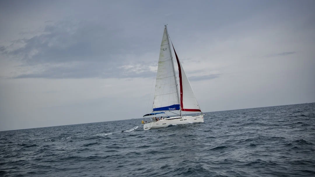 Sailboat navigating choppy blue ocean waves under overcast sky