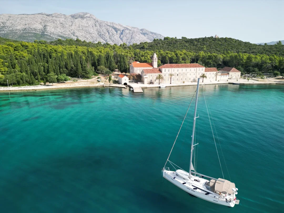 A sailboat anchored in crystal-clear waters near a small Croatian island surrounded by pine trees