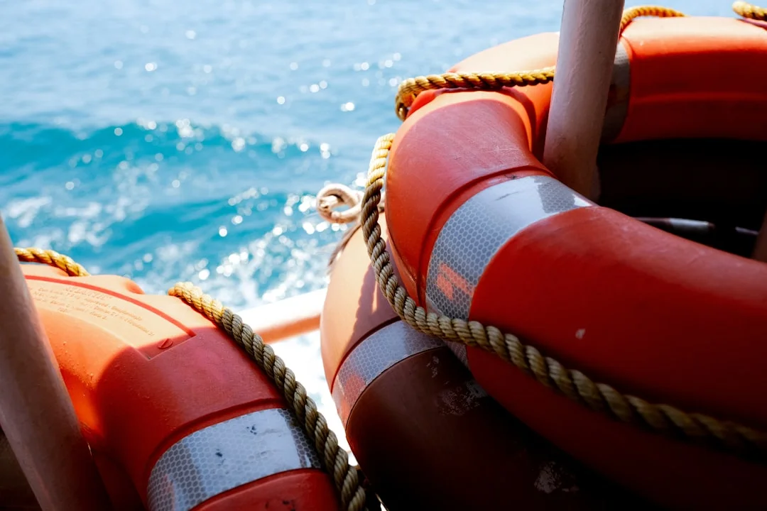 Person wearing an orange life jacket while seated in a sailing dinghy