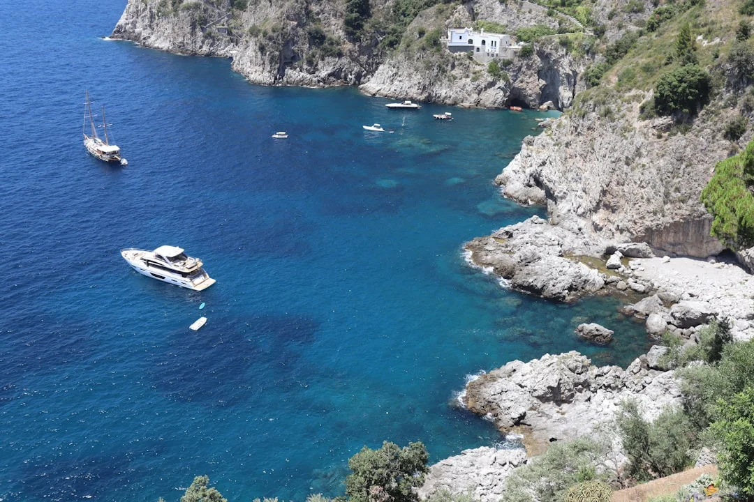 Two boats moored near towering sea cliffs along the Italian coastline