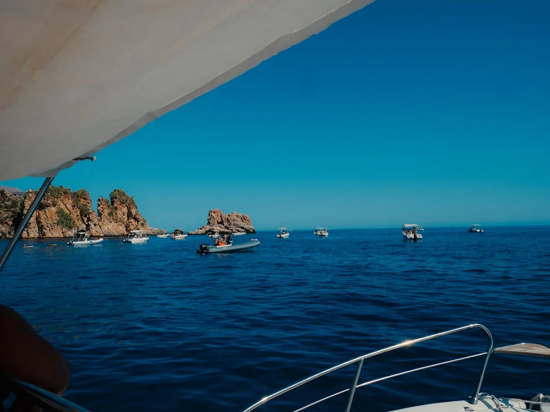 Several boats anchored in a calm turquoise bay surrounded by rocky islands on a summer afternoon