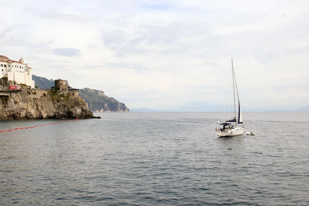 A sailing boat cruising along the Amalfi Coast with colorful cliffside villages in the background