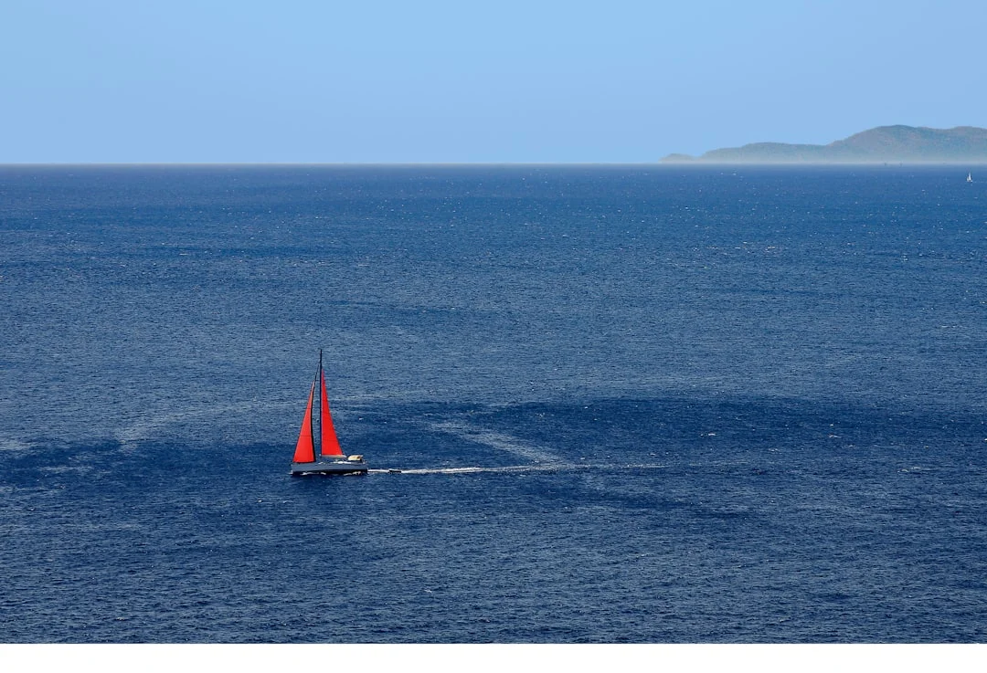 A red sailboat with the headsail unrolled, offshore at sea