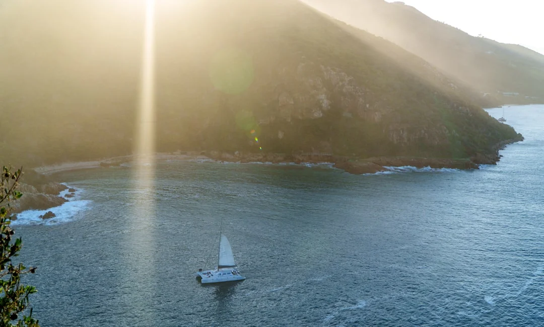 Used cruising sailboat at sunset along rocky coastline