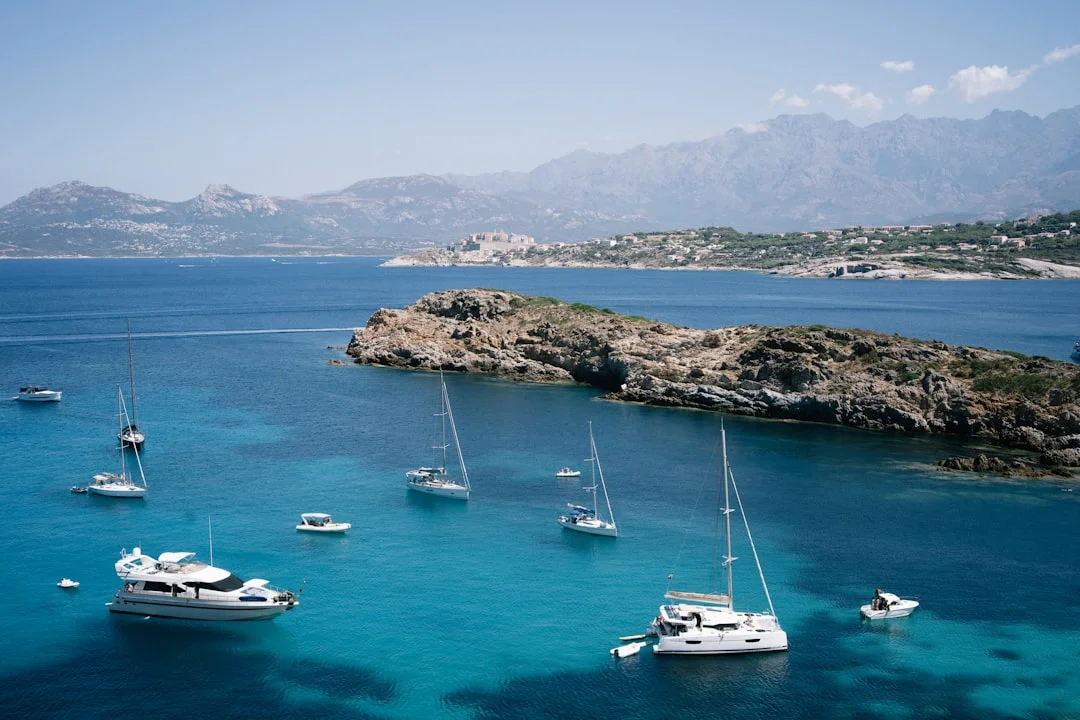 Several boats anchored in a calm turquoise bay surrounded by rocky islands on a summer afternoon
